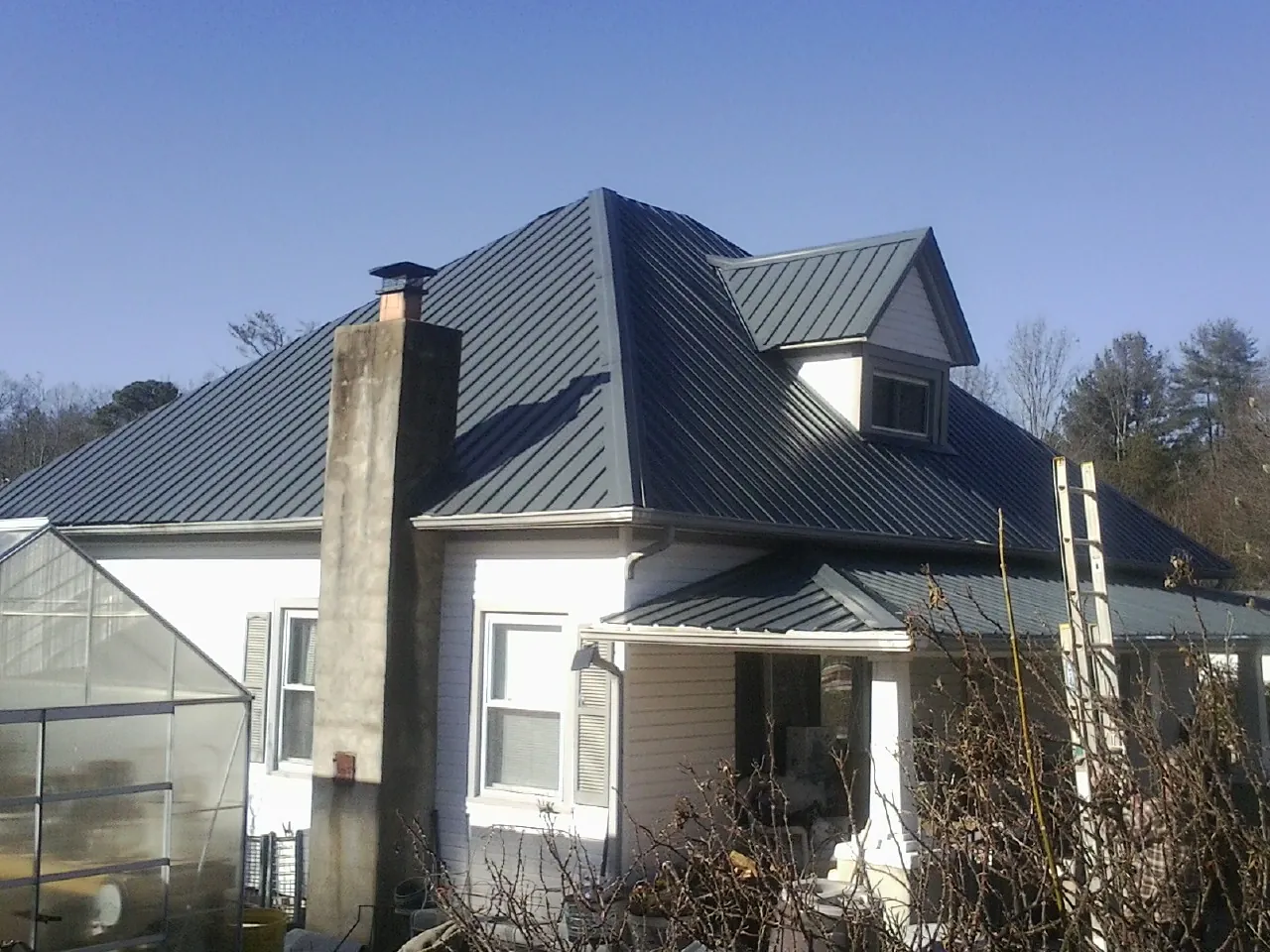 Dark blue standing seam metal roof on a white farmhouse with dormer — Slate & Tile Roof Repair by Roofing Brothers in Southmont