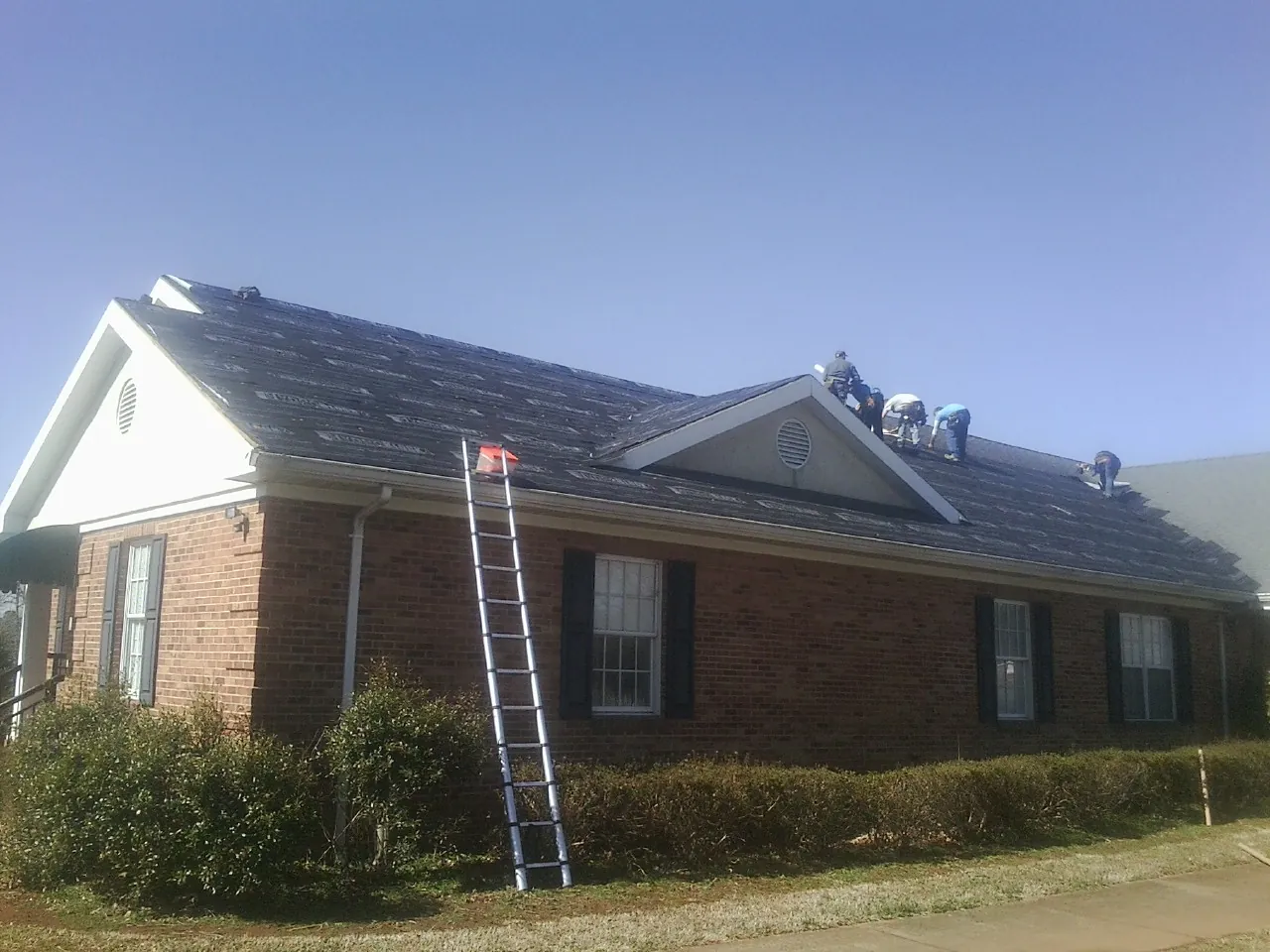 Crew tearing shingles off a brick ranch roof with a ladder set — Emergency Roof Repair work by our crew in Southmont