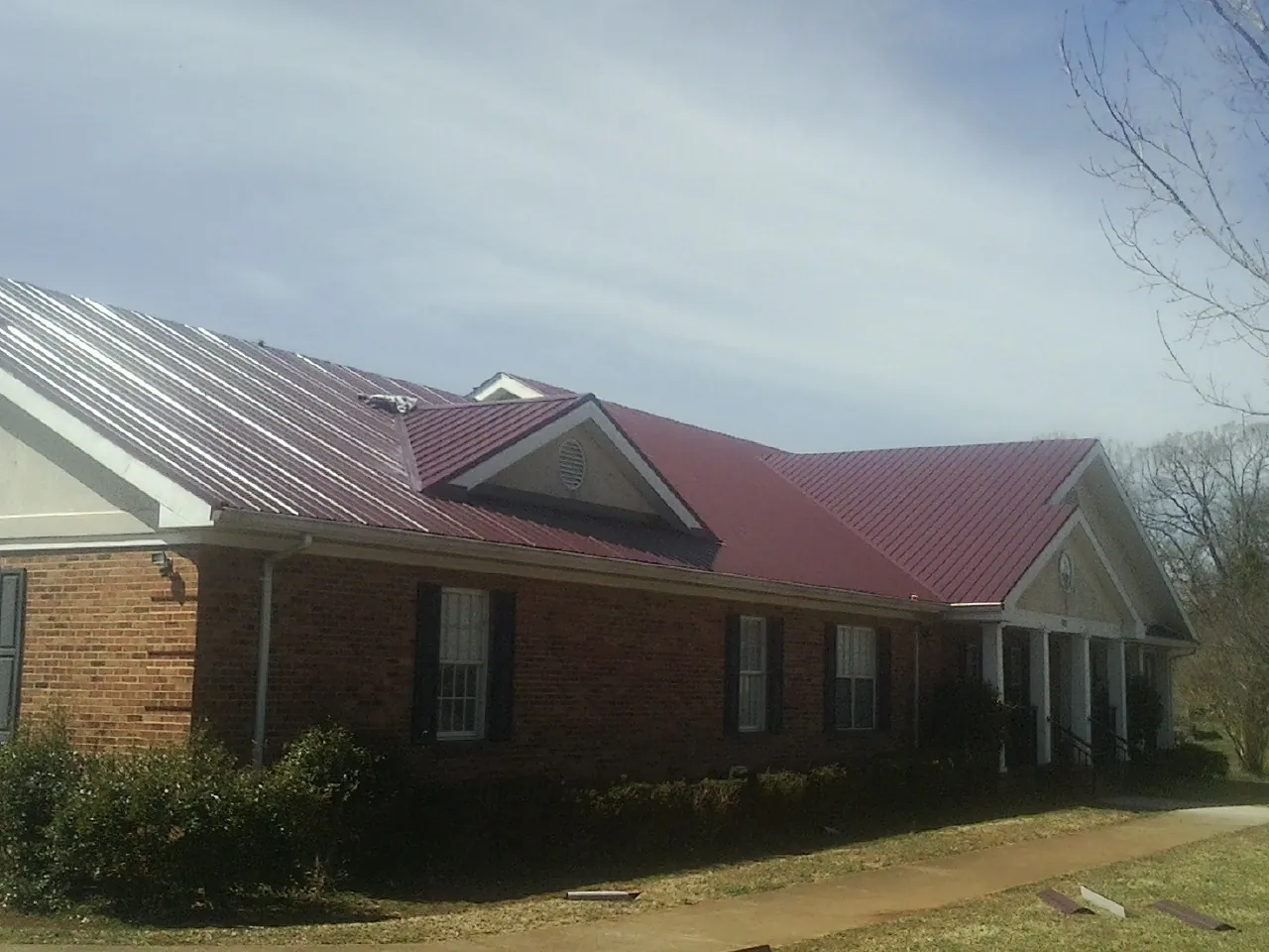 Red metal roof with gabled entries on a long brick building, from a Hail Damage Roof Repair job in Southmont