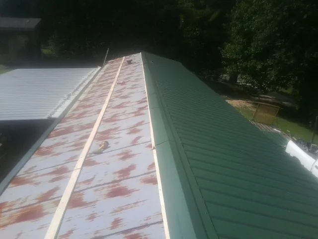 Old rusted panels beside newly installed green metal roofing — Wind Damage Roof Repair by Roofing Brothers in Southmont
