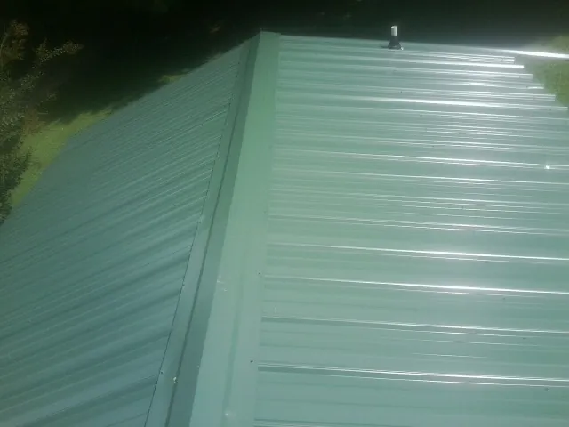 New green metal panels meeting at the ridge of a roof — Flat Roof Repair work by our crew in Southmont