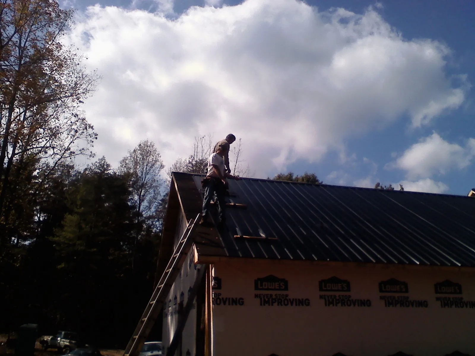 Roofer fastening dark metal panels high against a cloudy sky, from a Roof Inspection job in Southmont