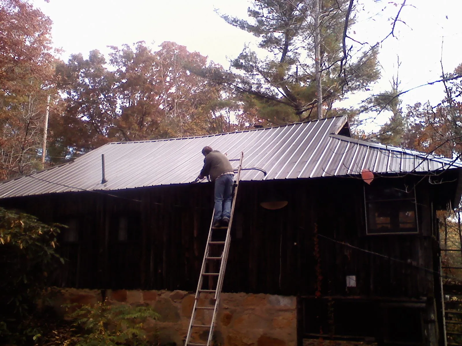 Roofer on a ladder working along the edge of a cabin metal roof in Southmont