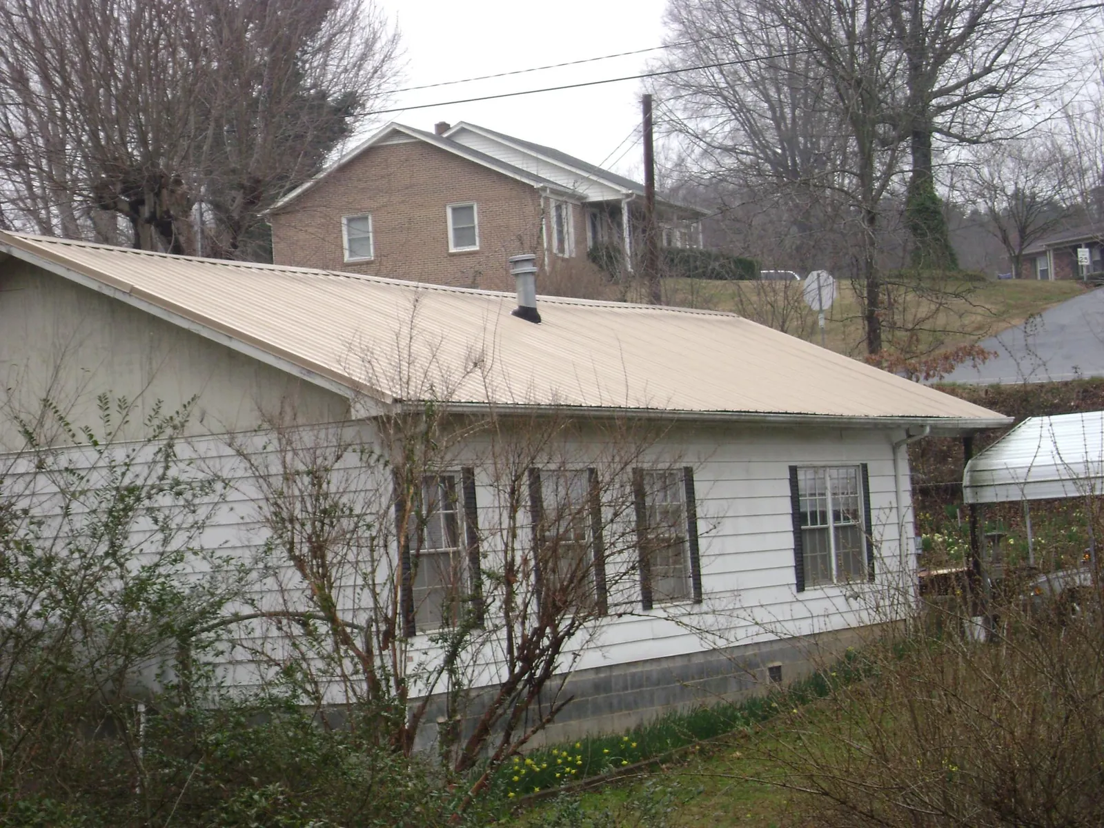 Tan metal roof on a white sided house set into a hillside — Commercial Roofing by Roofing Brothers in Southmont