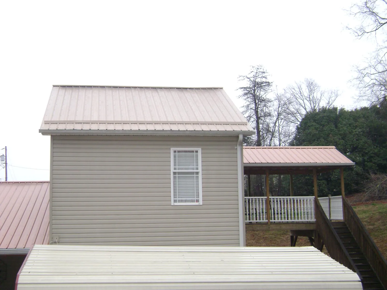 Tan metal roofs on a two story addition and attached porch, from a Roof Replacement job in Southmont